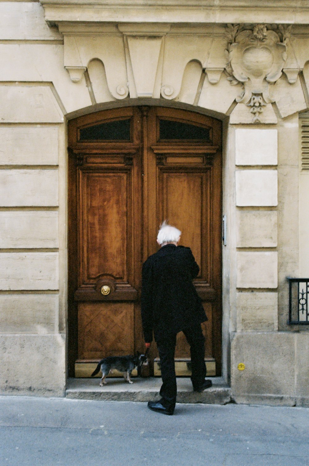 man in black coat standing beside brown wooden door