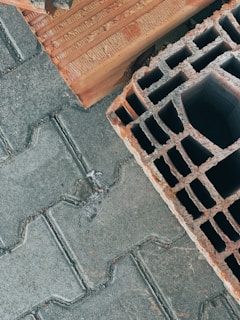 Concrete pavers are laid in a herringbone pattern beside a large, hollow, red clay brick. The textures of both materials are prominent, showing detailed grooves and rough surfaces.