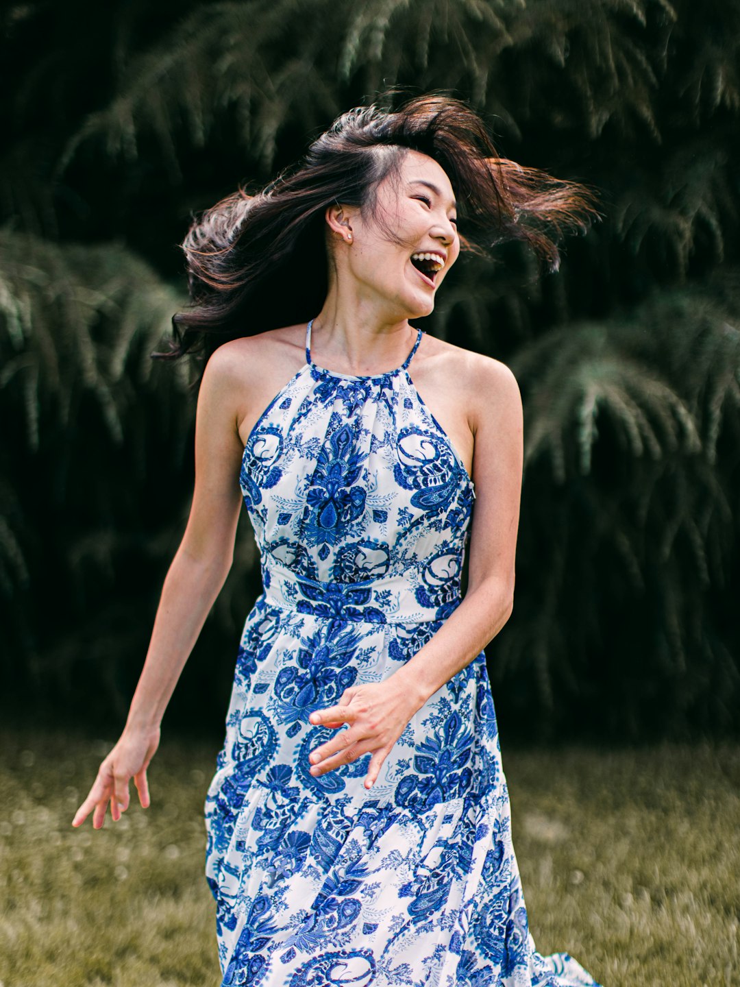 woman in blue and white floral spaghetti strap dress standing on green grass field during daytime