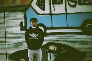 A proud Detroit worker wearing a Detroit Grit City hoodie, standing in front of a mural.