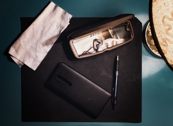 A flat lay of everyday essentials including glasses, a watch, and a smartphone on a light wooden surface.