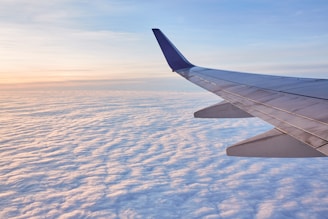 A bright airplane wing soaring above fluffy white clouds at sunrise.