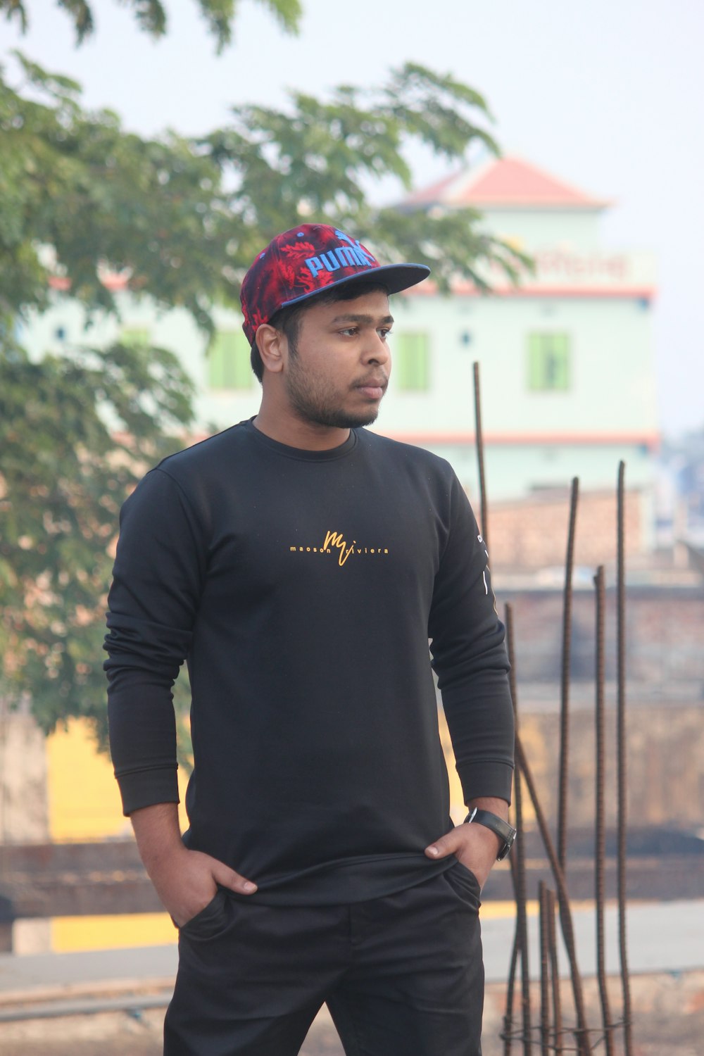 man in black long sleeve shirt and red cap standing near brown wooden fence during daytime