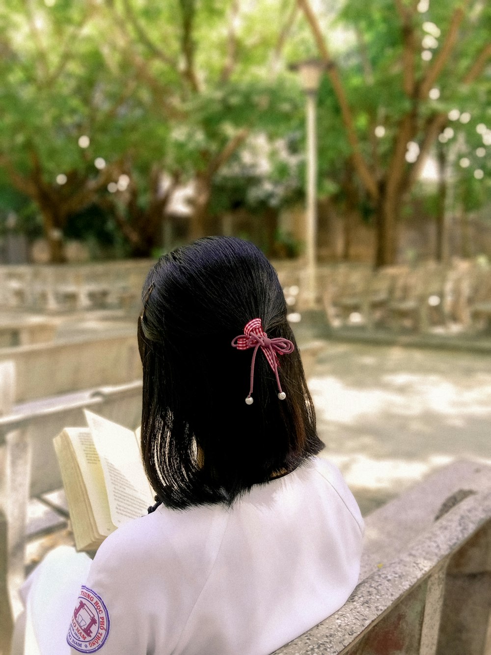 woman in white shirt and red hair tie sitting on bench reading book during daytime