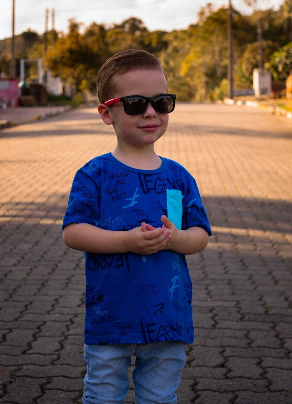 boy in blue crew neck t-shirt wearing brown sunglasses standing on sidewalk during daytime