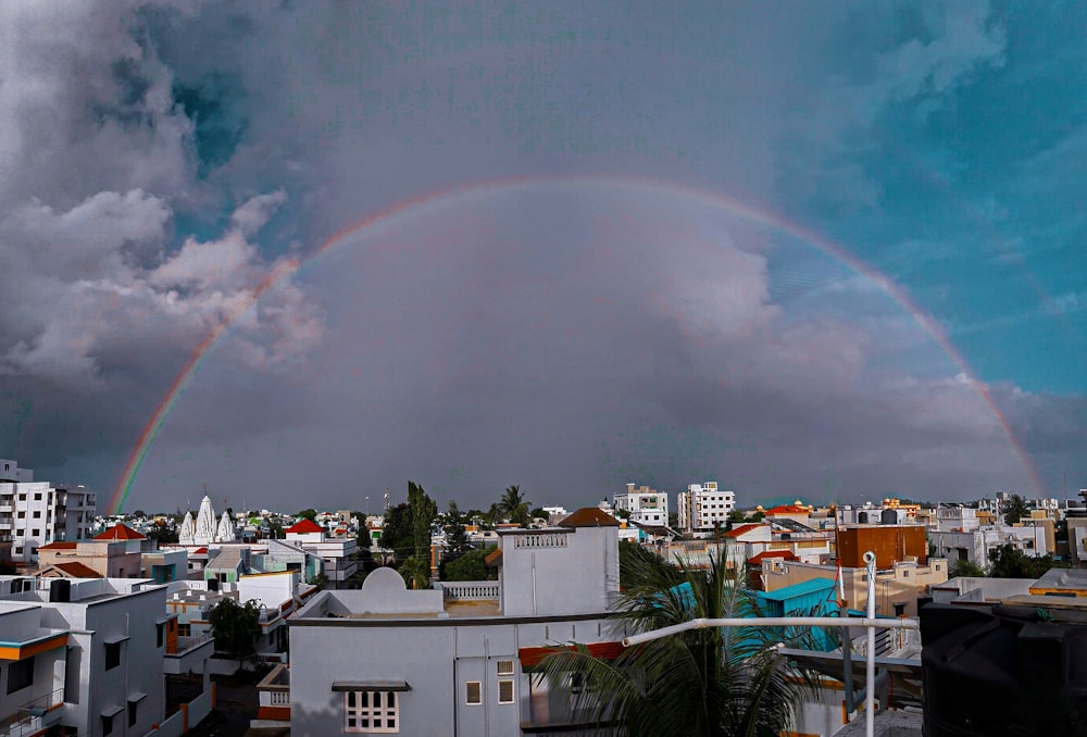 rainbow over city with buildings and trees under gray cloudy sky