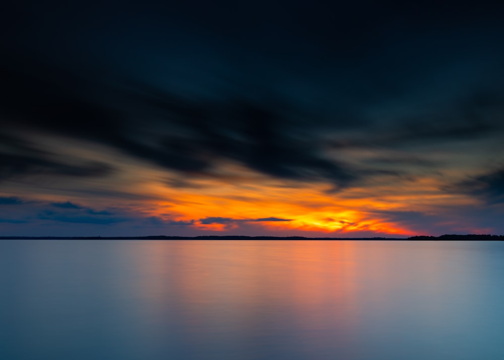 Cuerpo de agua bajo cielo nublado durante la puesta del sol