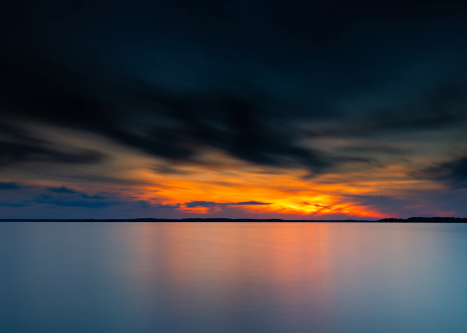 Serene sunset over water with vibrant orange and blue hues in the background