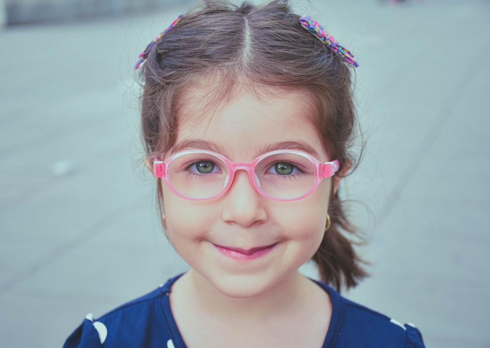 Fille en chemise bleue et blanche portant des lunettes à monture rose