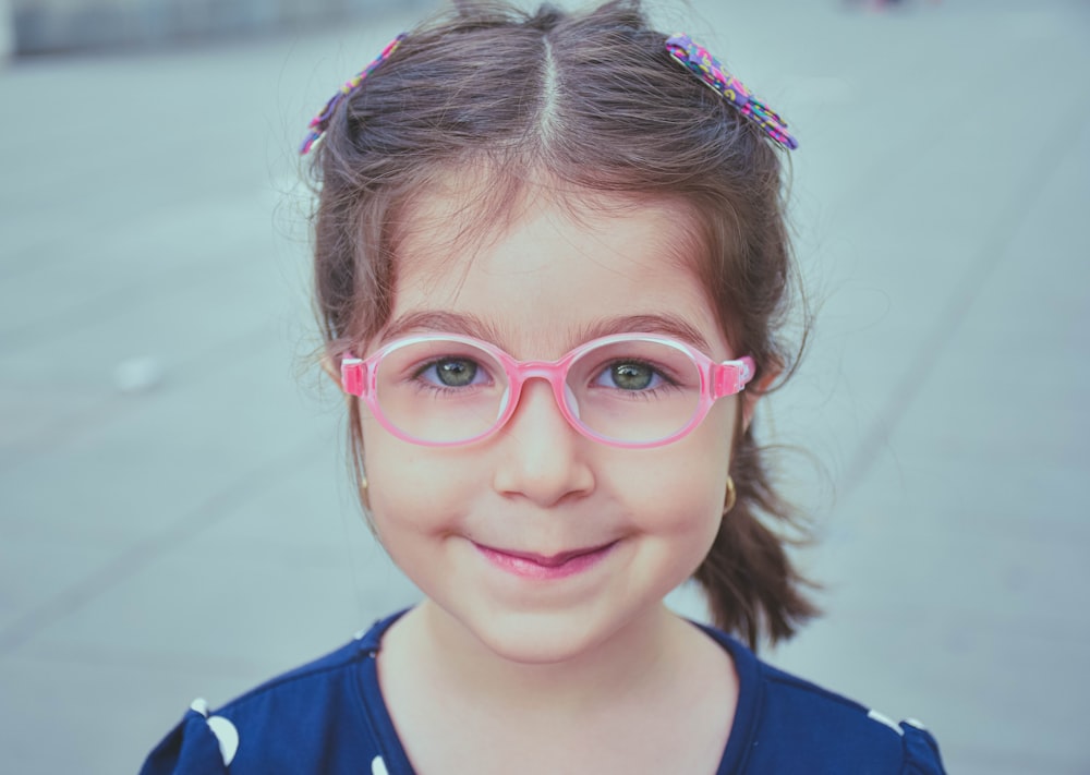 girl in blue and white shirt wearing pink framed eyeglasses