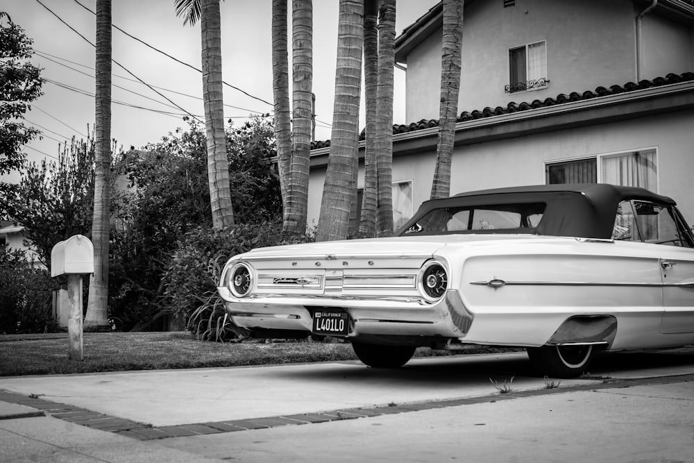 grayscale photo of classic car parked beside building