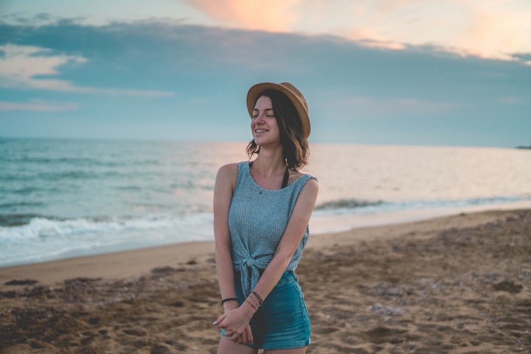 woman in blue tank top and blue denim shorts standing on beach shore during daytime