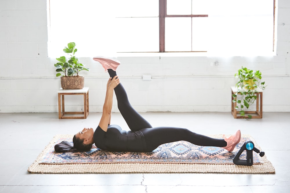 woman in black tank top and black leggings lying on black and white floral area rug