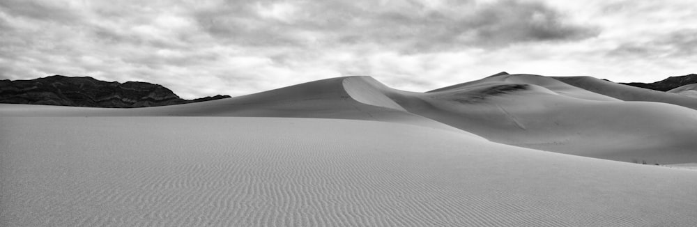 grayscale photo of desert under cloudy sky