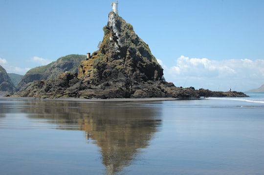 white lighthouse on brown rock formation near body of water during daytime in Whatipu Beach New Zealand