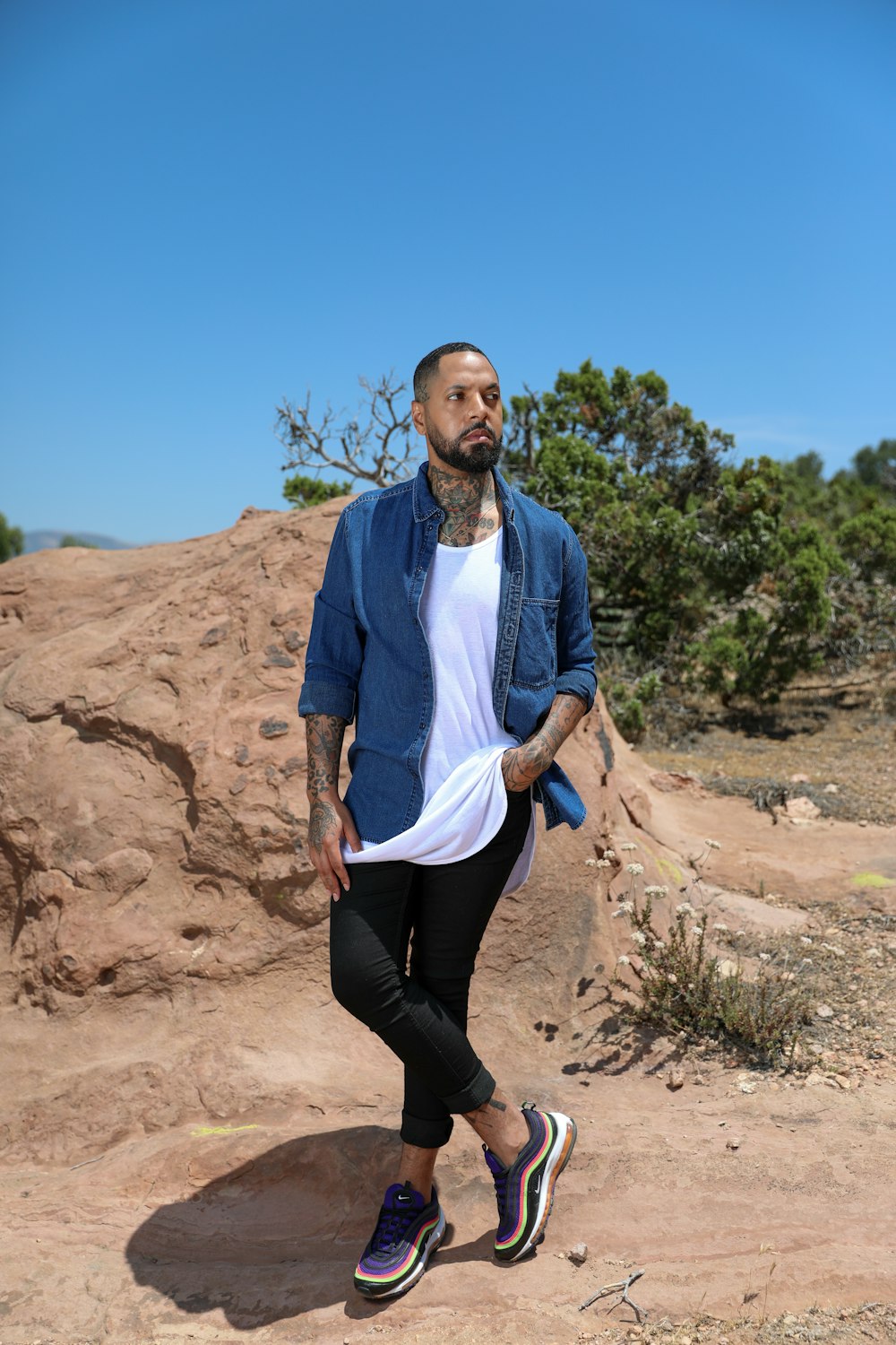 man in blue dress shirt and black pants sitting on brown rock during daytime