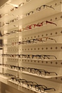 Shelves display various styles and colors of eyeglasses arranged neatly in rows against a white background with perforated holes.