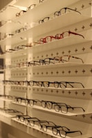 Shelves display various styles and colors of eyeglasses arranged neatly in rows against a white background with perforated holes.