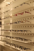 Shelves display various styles and colors of eyeglasses arranged neatly in rows against a white background with perforated holes.