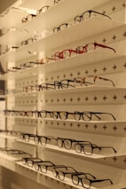 A clean, modern display of various stylish optical frames arranged neatly on glass shelves.