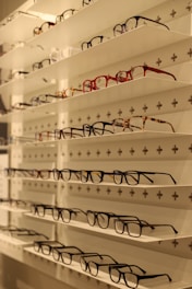 Shelves display various styles and colors of eyeglasses arranged neatly in rows against a white background with perforated holes.