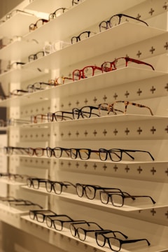Shelves display various styles and colors of eyeglasses arranged neatly in rows against a white background with perforated holes.