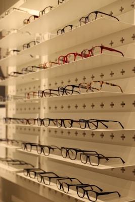 Display of various eyeglass frames arranged neatly on a minimalist shelf.