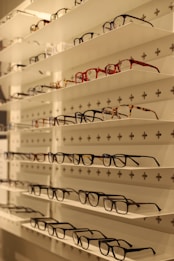 Shelves display various styles and colors of eyeglasses arranged neatly in rows against a white background with perforated holes.