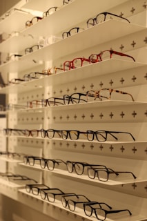 Shelves display various styles and colors of eyeglasses arranged neatly in rows against a white background with perforated holes.
