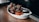 A white dish containing pieces of crispy, glazed chicken wings garnished with green herbs. Accompanied by carrot and celery sticks, along with a small black container of dipping sauce. The wooden table adds a rustic feel.