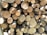 A stack of cut logs with various diameters, neatly arranged and displaying the cross-sections of tree trunks. The wood varies in color from light beige to darker brown, indicating freshly cut timber with visible growth rings and some rough bark edges.
