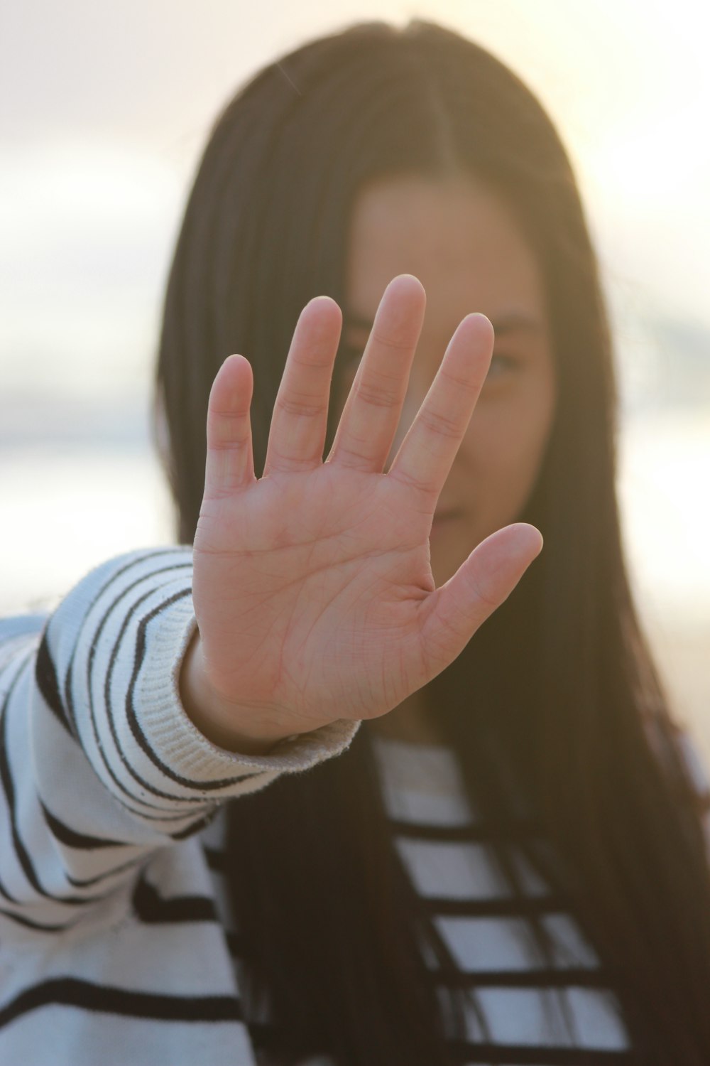 白と灰色の縞模様の長袖シャツを着て、手で顔を覆っている女性