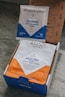 Two packages of coffee from Klatch Coffee are displayed. One is a small packet labeled 'Colombia Roasters United Blend' with a blue and white design. The other is a larger bag labeled 'Mocha Java Blend' with a blue and orange design. Both packages are situated inside an open cardboard box with printed text and graphics.