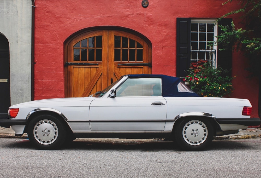white convertible car parked beside brown concrete building during daytime
