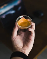 A hand holding a perfectly pulled espresso shot with rich crema in a small glass.