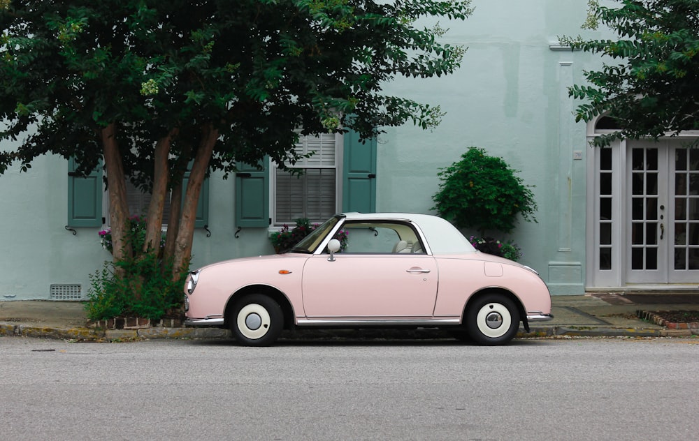 coupé rosa e bianca parcheggiata accanto agli alberi verdi durante il giorno