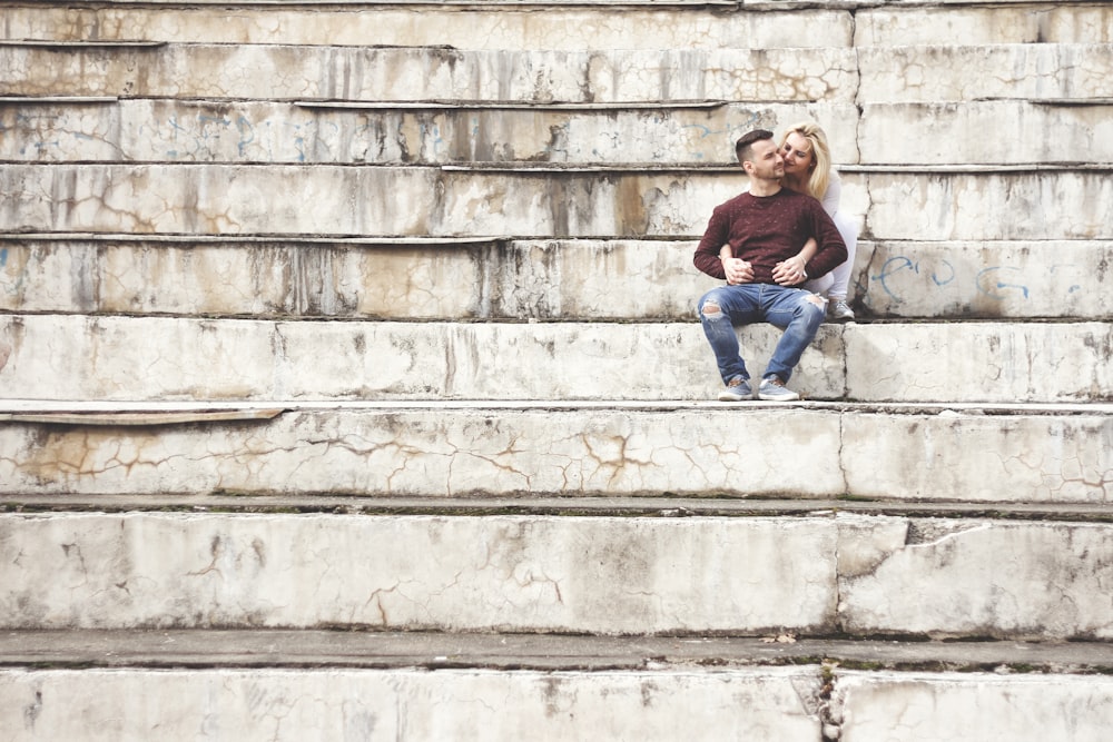 woman in pink long sleeve shirt and blue denim jeans sitting on gray concrete stairs