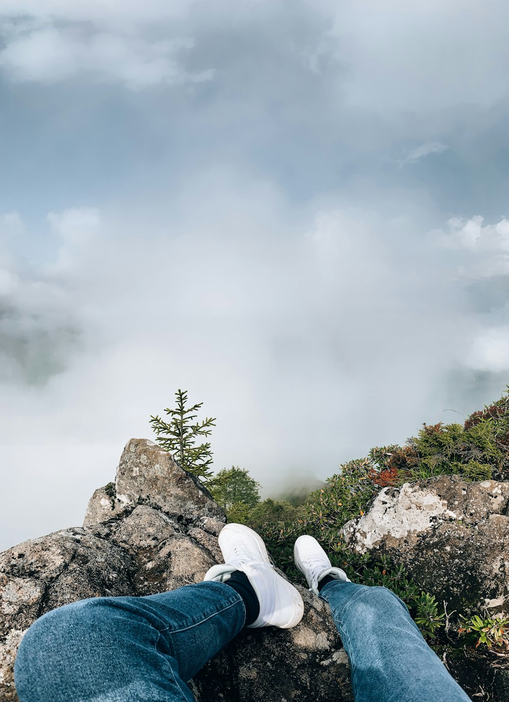 person in blue denim jeans and white sneakers sitting on rock