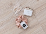 A set of pearl hair clips, a bar of natural handcrafted soap, and a beige satin scrunchie arranged on a light wood surface. The soap is labeled with 'JONK' and mentions scents of guido and eucalyptus.