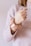 A hand wearing a pink scrunchie is visible, with the arm covered in a soft, light pink sweater. The hand has a ring on the ring finger.