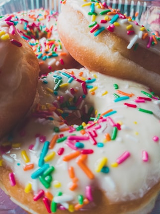 A close-up of several glazed donuts covered in colorful sprinkles, highlighting the texture of the icing and the vibrant colors of the toppings.