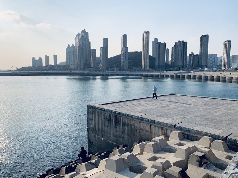 person in black jacket and black pants standing on gray concrete dock during daytime