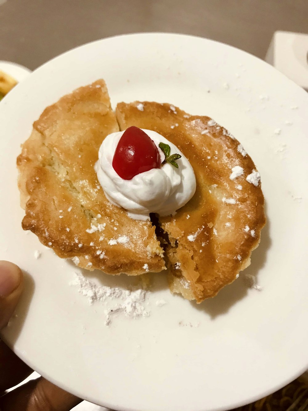 person holding white ceramic plate with brown pastry