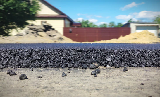 Close-up of heavy equipment laying asphalt on a rural road under clear skies.