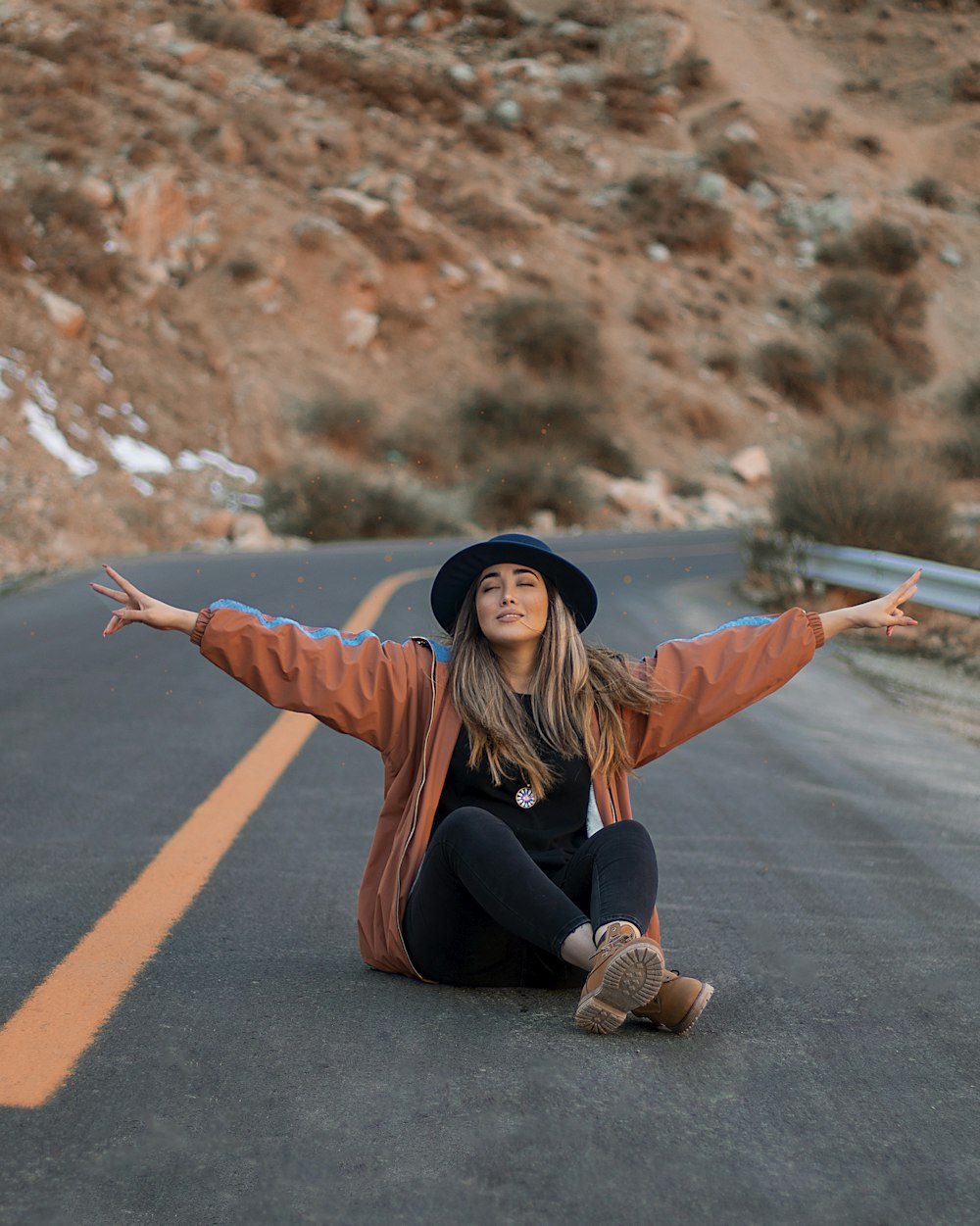 woman in orange long sleeve shirt and black hat sitting on road during daytime