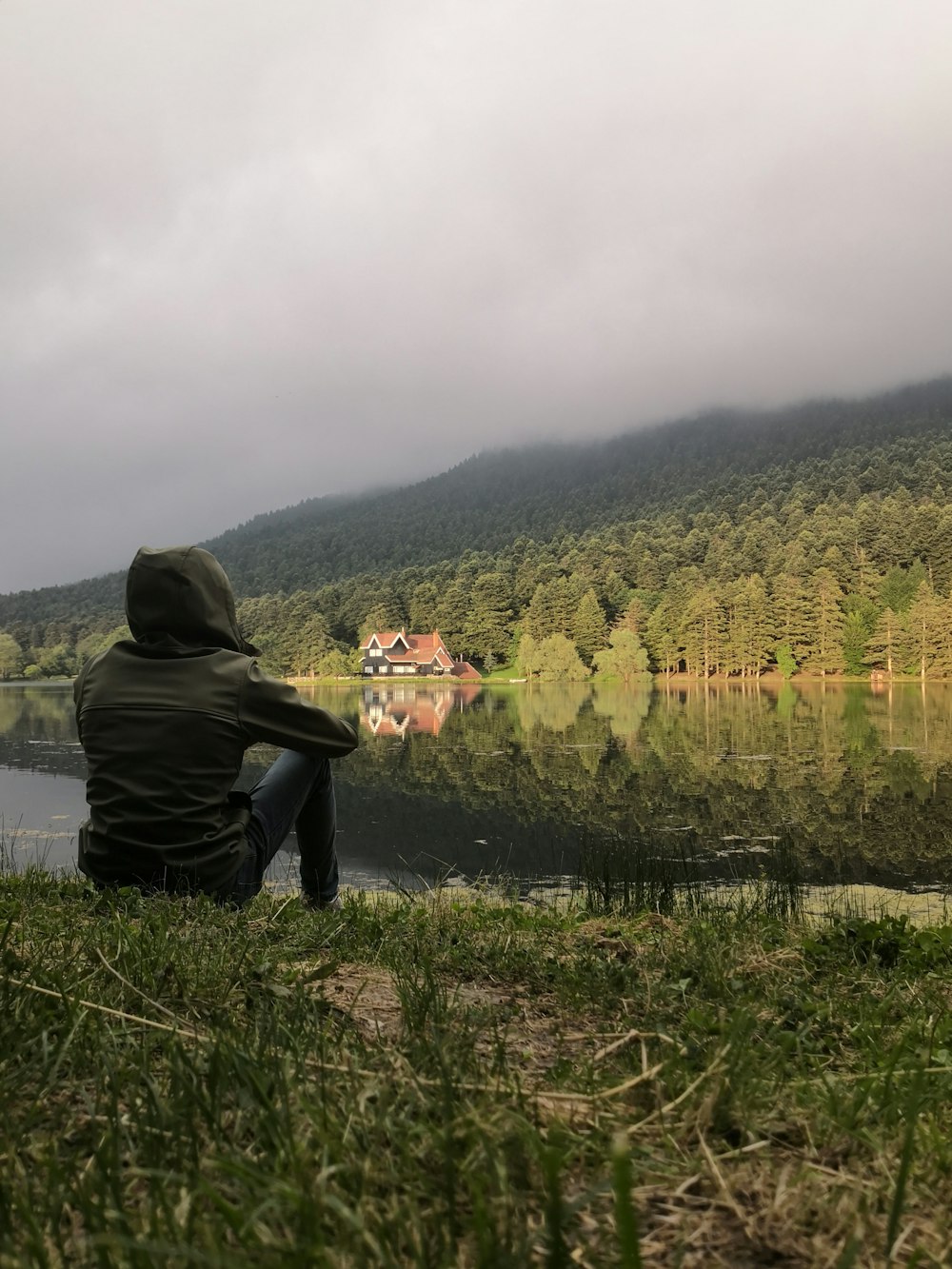 Persona con sudadera con capucha negra de pie cerca del lago durante el día
