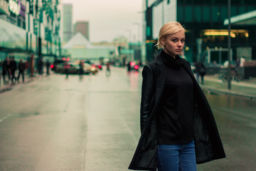 woman in black jacket standing on sidewalk during daytime