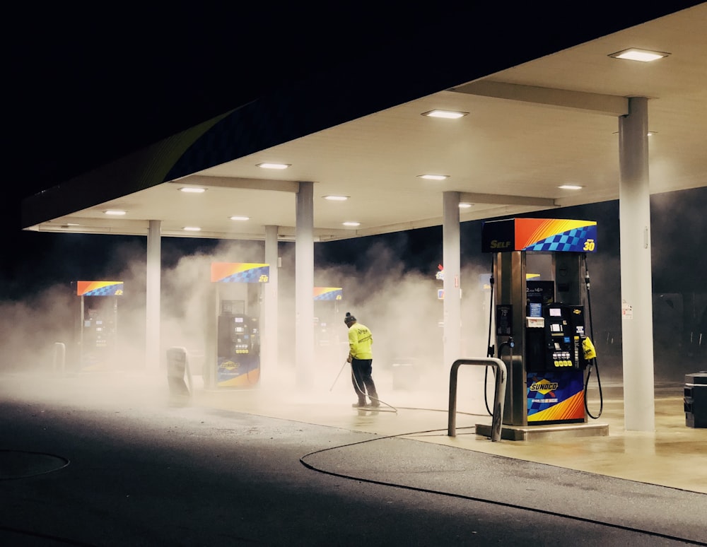 hombre con chaqueta amarilla de pie cerca de la bomba de gasolina