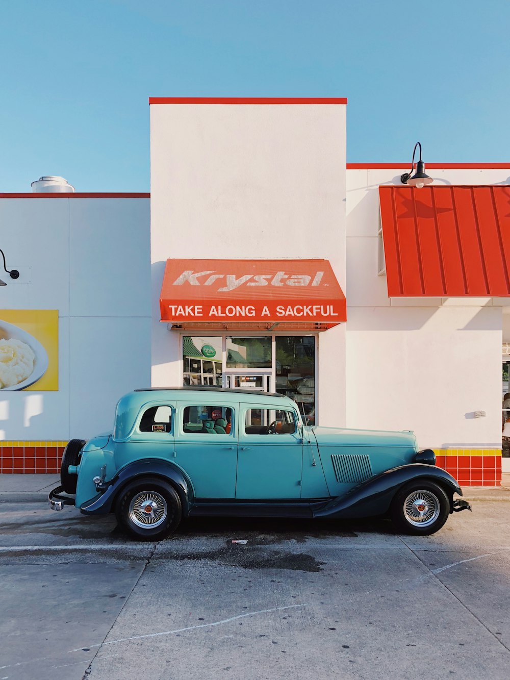 teal and white vintage car parked beside white and red concrete building during daytime