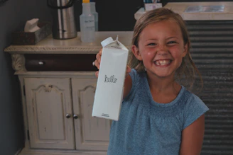 A smiling child holding a handmade thank-you card in a sunlit community center.